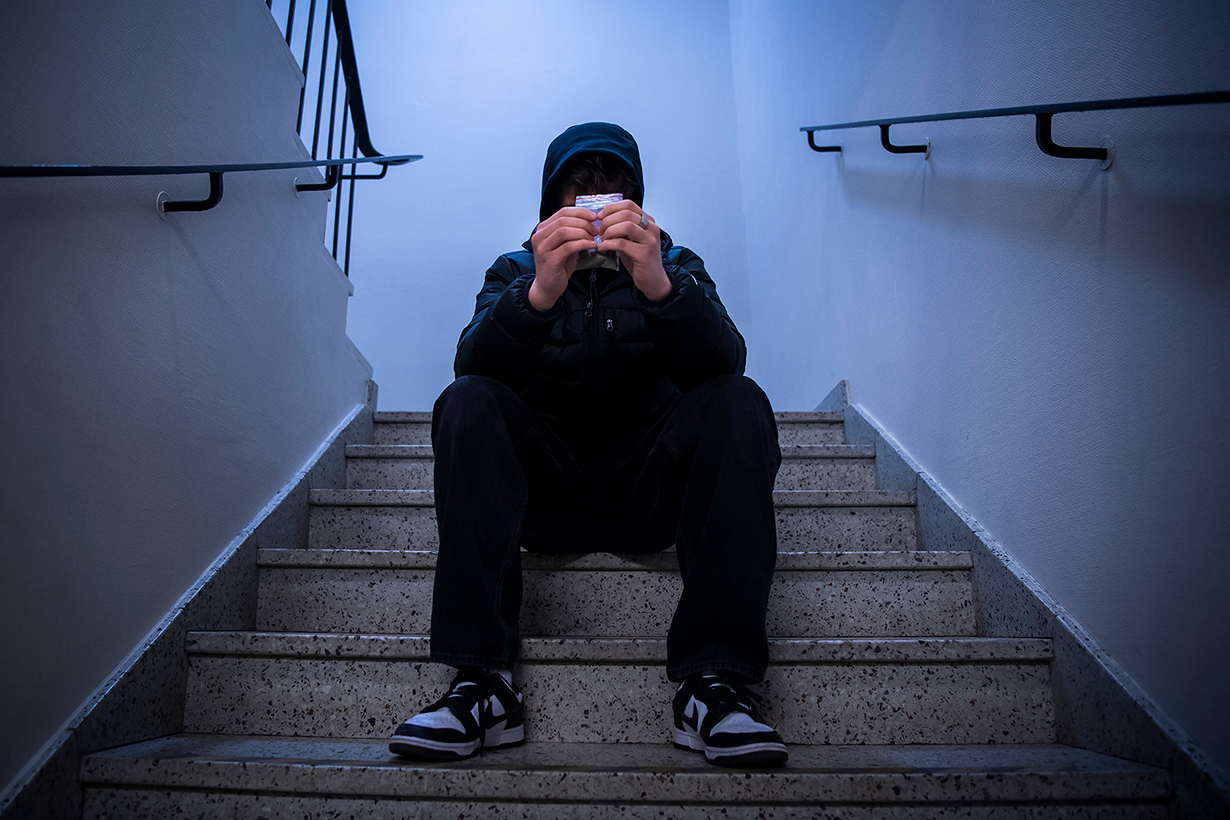 En ung gutt i mørke klær sitter i en trappeoppgang med en liten pose i hendene.