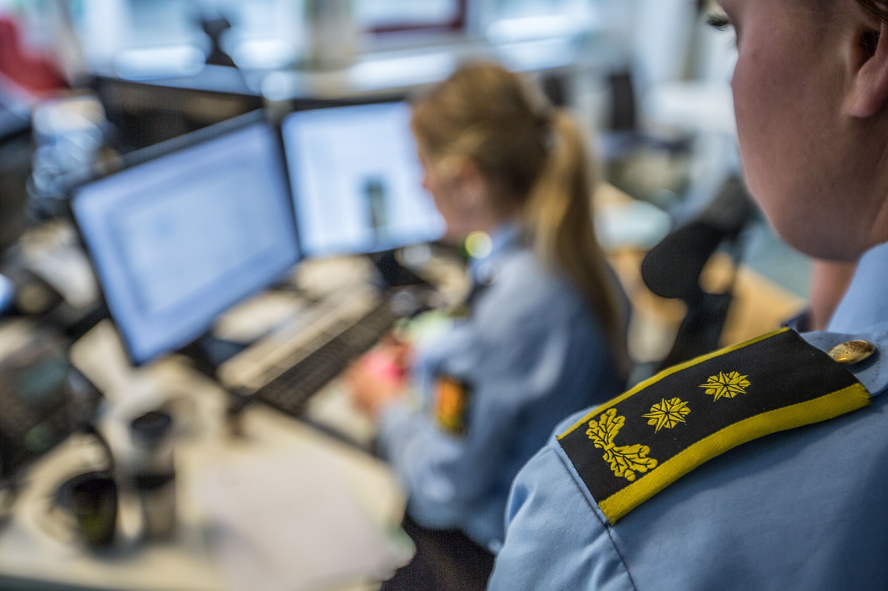 Skulderen og siden av et ansikt. Dame i politiuniform foran pc, blurret i bakgrunnen.