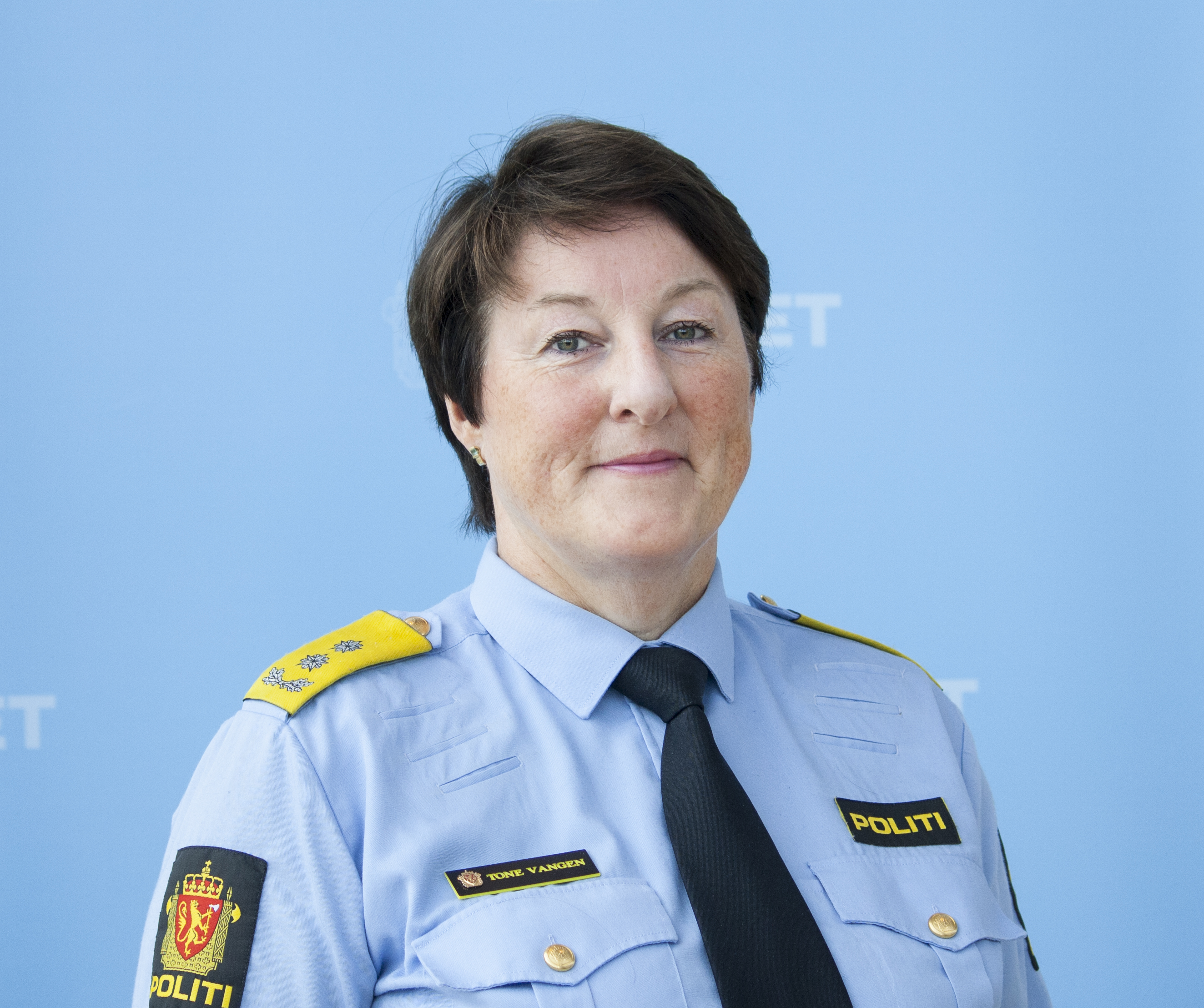 kvinnelig leder i politiet står foran en blå vegg med politiets våpenskjold på. Kvinnen har kort brunrødt hår og er i 50-årene. 
