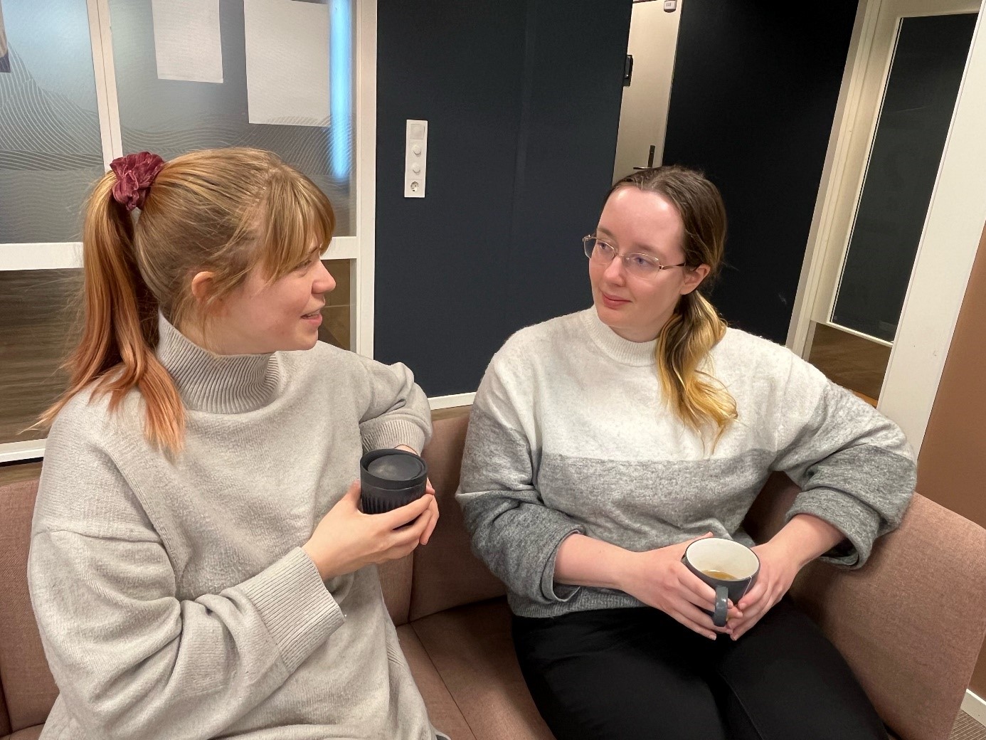 Kristine sitter i en sofa på jobbe med en kopp kaffe. Her snakker hun med Tita.
