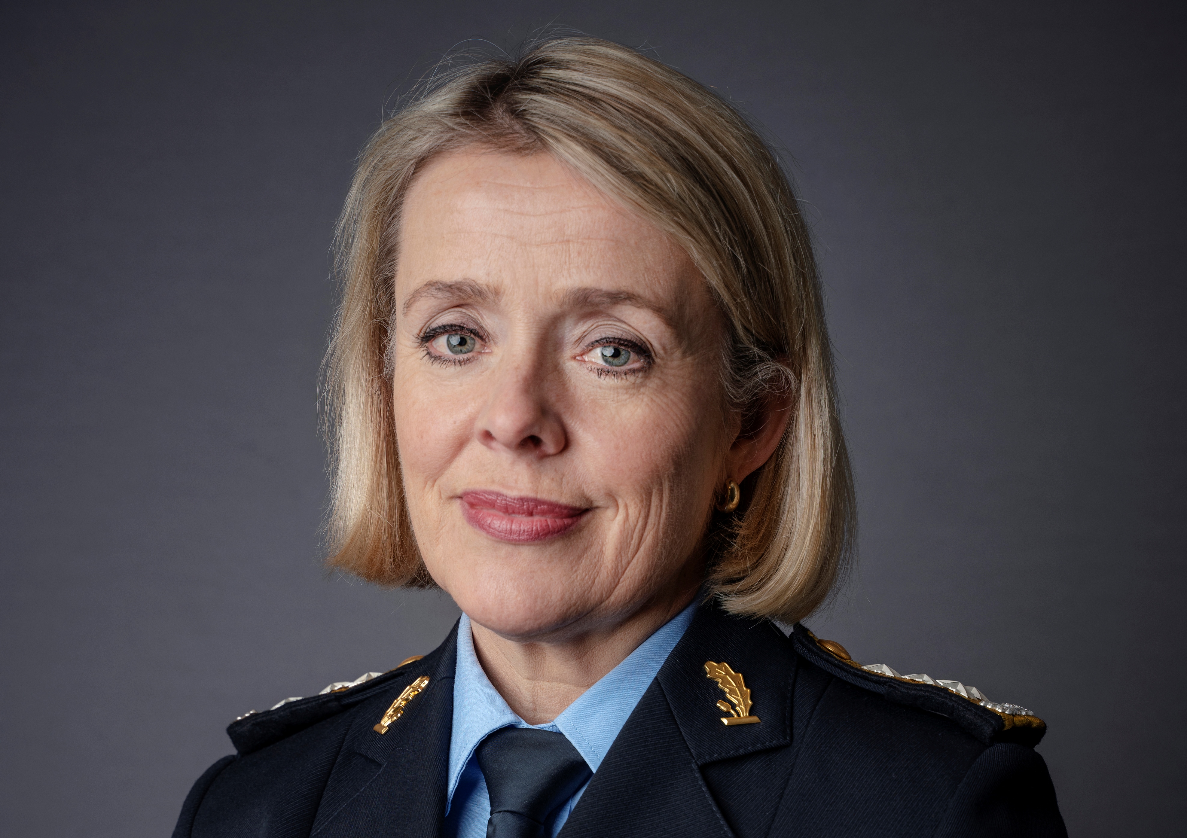 Bilde av kvinnelig politi i mørk jakke og kort lyst hår.