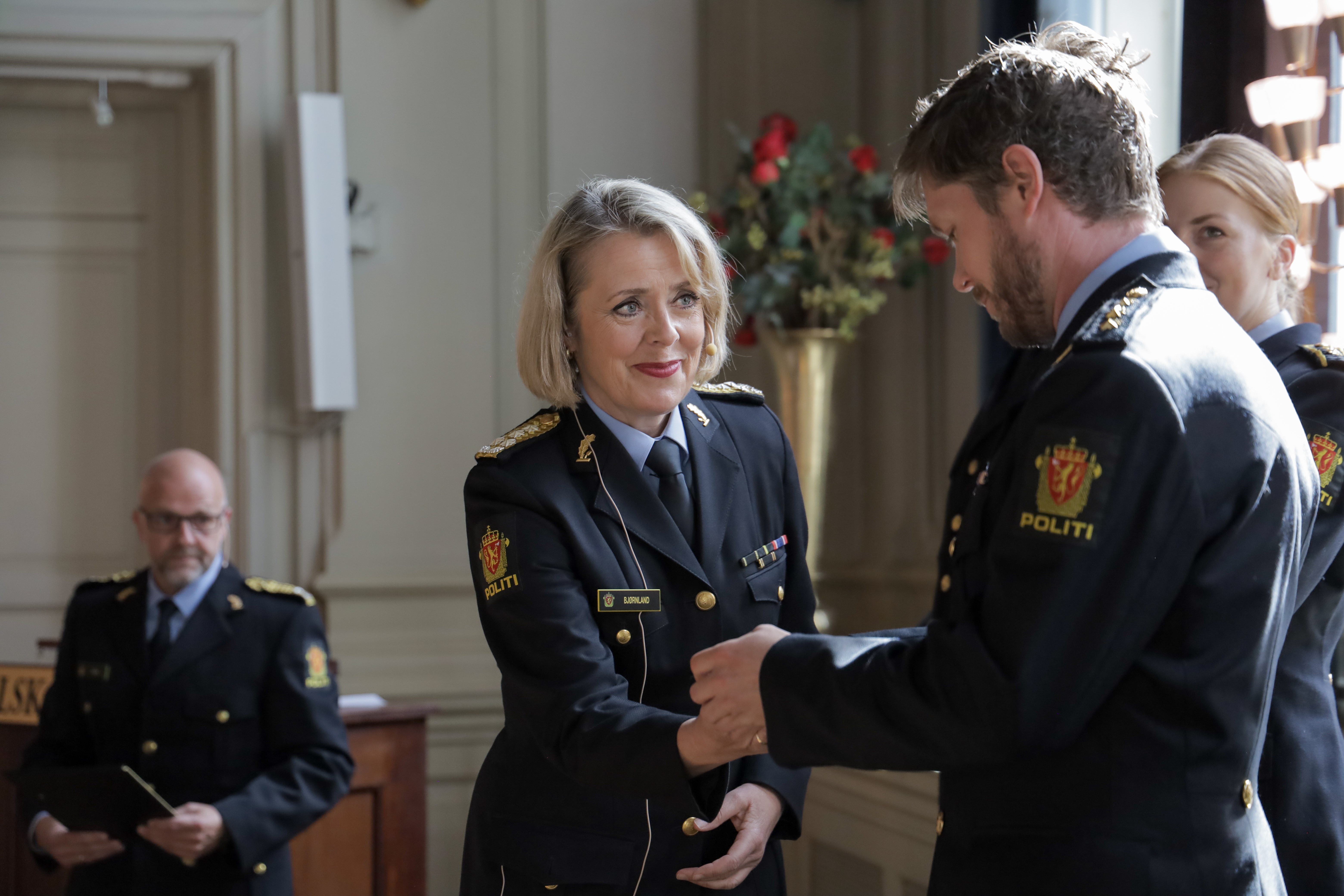 En politikvinne i svart uniform smiler i det hun overrekker en medalje til en mannlig politibetjent.