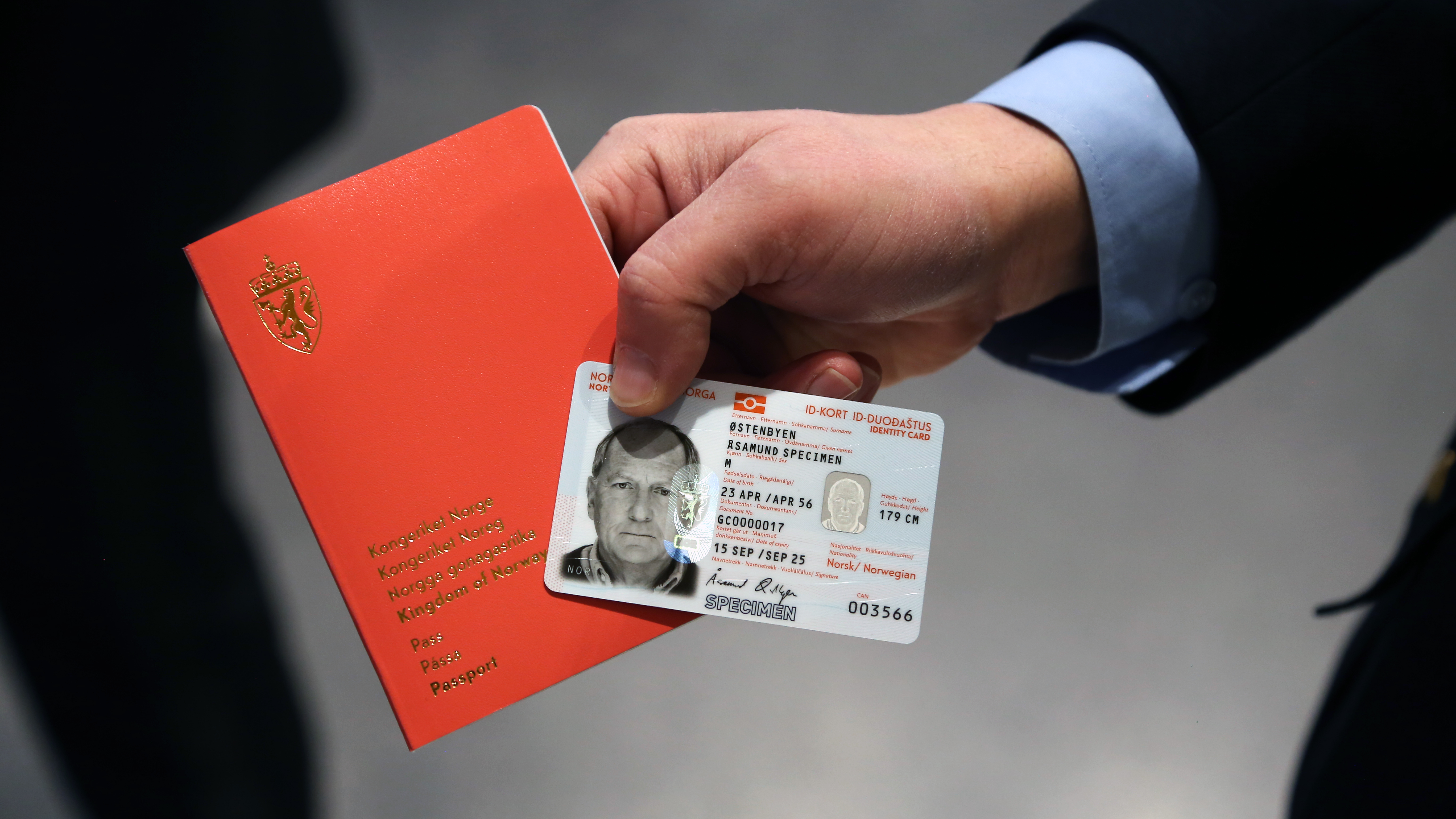Bilde av et rødt norsk pass og et norsk ID-kort i plastikk, holdt frem av en mannlig hånd.