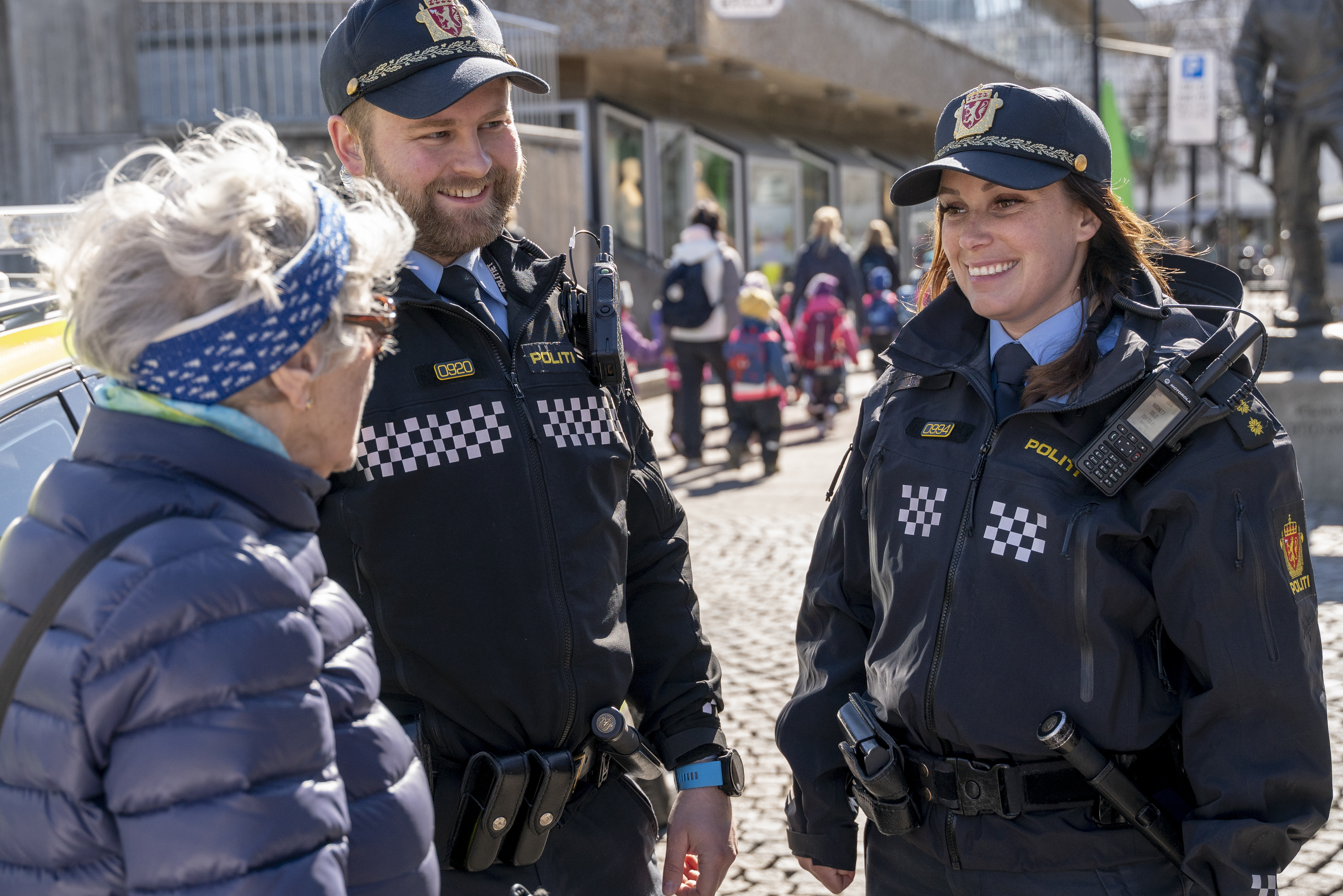 To politifolk står på en solfyllt gate og samtaler med en eldre kvinne