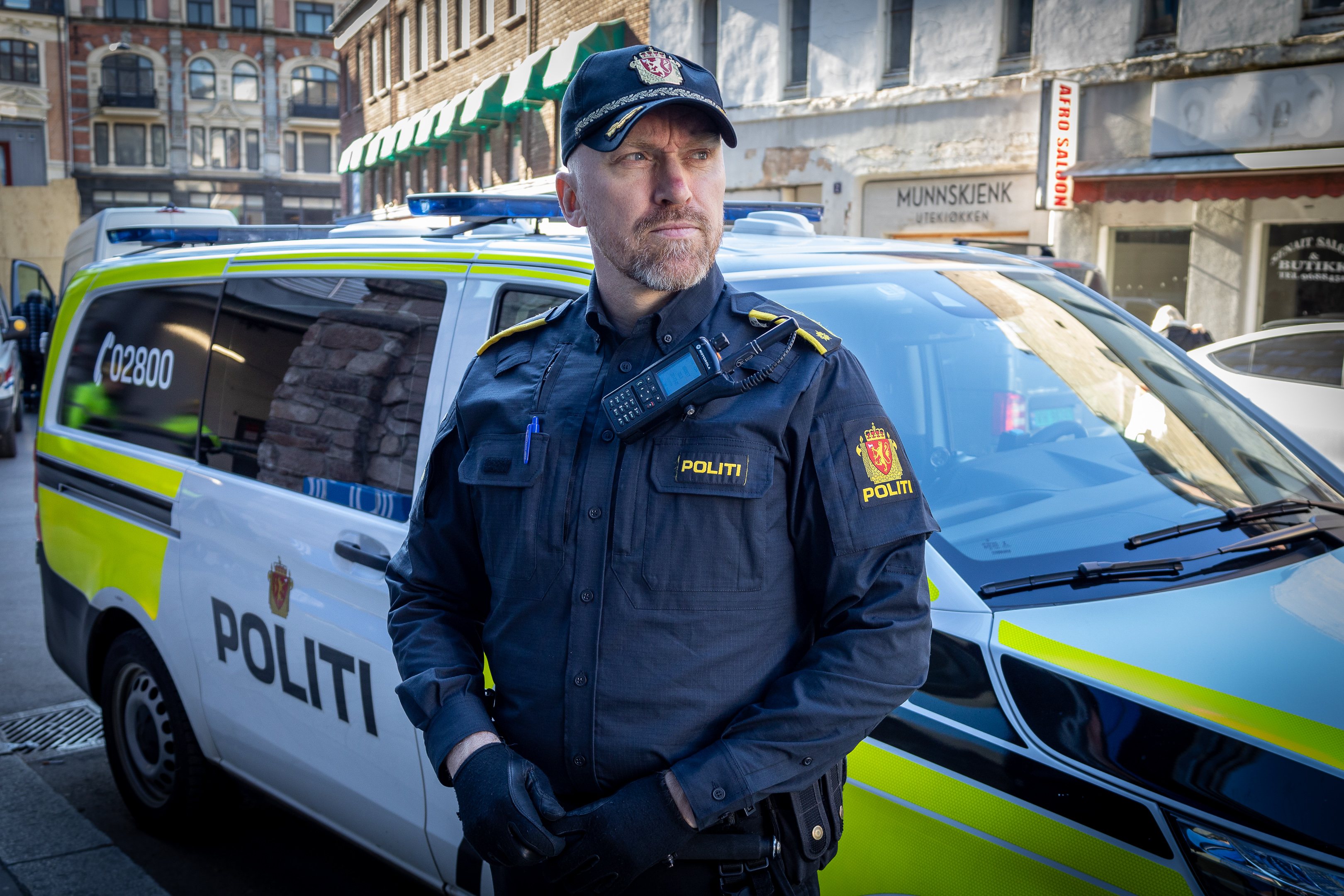Politimann med arbeidsskjorte foran politibil.